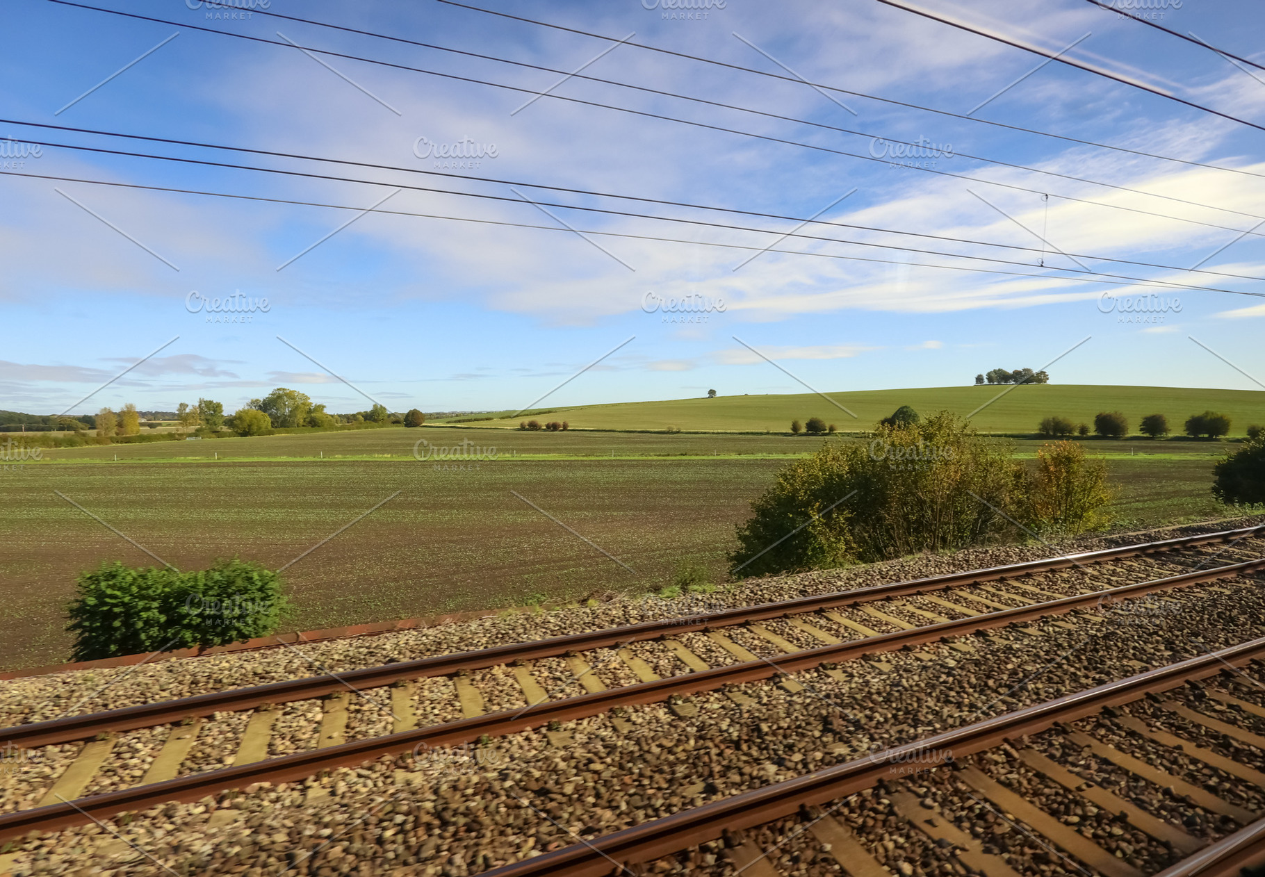 Railway tracks passing through green rural landscape under blue, a Photo by Studio ANNA
