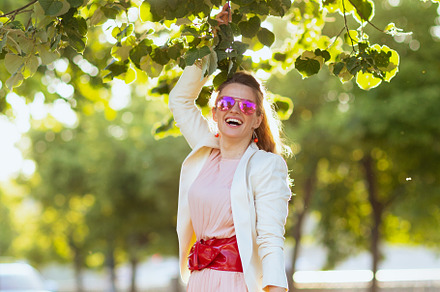 smiling trendy woman in pink dress and white jacket in city, a Person Photo by Alliance Images