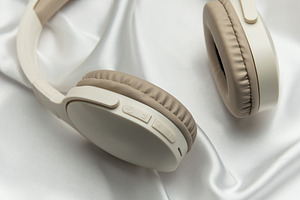 Modern wireless headphones lying on white silk background, a Technology Photo by Olena Rudo