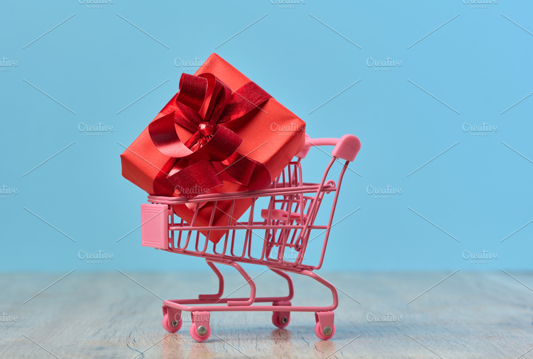 A gift wrapped in red paper in a miniature shopping cart on a bl, a Holiday Photo by ndanko
