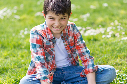 Boy sitting on grass picking daisies in a sunny park., a Person Photo by RF Images