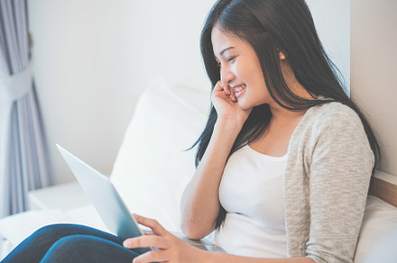 Young woman working on a laptop sitting on bed at home, a Person Photo by Casanowe-studio