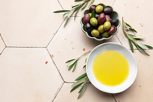 Olive oil and olives with olive branches resting on a tiled surf, a Food & Drink Photo by Olena Rudo