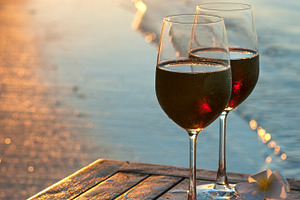 Romantic beach scene: two glasses of red wine at sunset near water