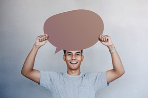 Smiling man holding blank speech bubble in studio. Positive conc, a Photo by salmon.black
