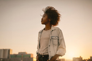 Black woman standing at sunset with city skyline, a Photo by DanFLCreativo