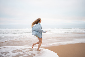 Carefree woman in casualwear running on wet seashore at beach, a Photo by andreonegin market