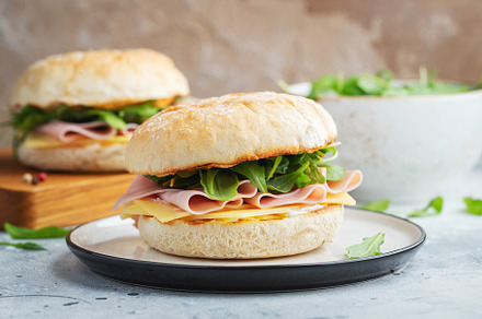 Two homemade sandwiches with ham, cheese and arugula on a concrete table., a Food & Drink Photo by Budarinphoto