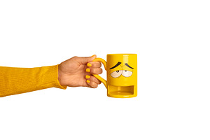 Hand holding a yellow mug with a sad face design, matching yello, a Food & Drink Photo by Ales Munt