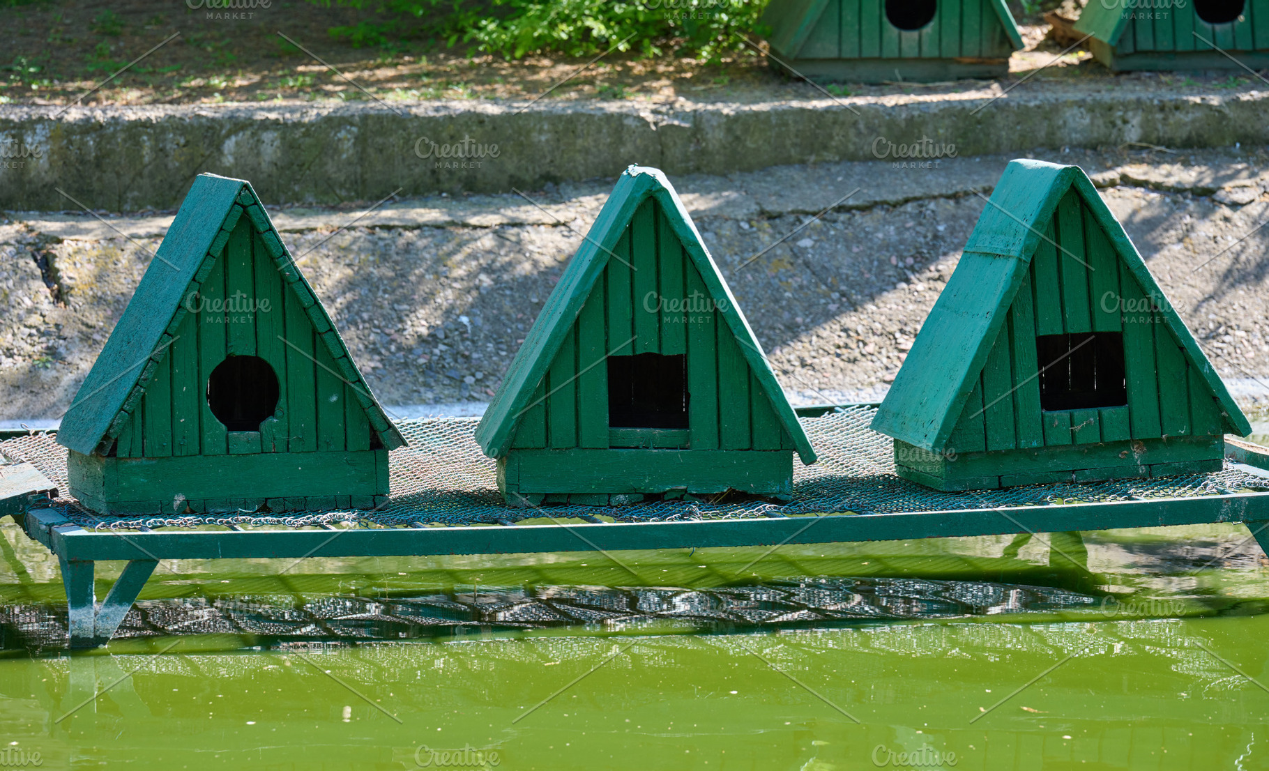Small green wooden birdhouses with triangular roofs, set on a gr, an Architecture Photo by ndanko
