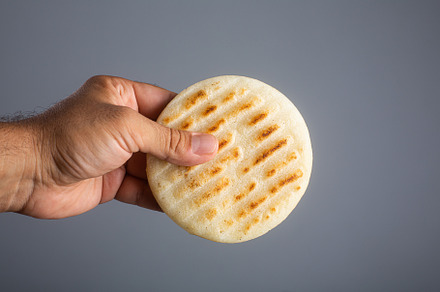 Man holds traditional Venezuelan food arepa made from cornmeal, a Food & Drink Photo by zakiroff