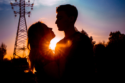 Silhouettes of a guy and girl in a field on a sunset background containing