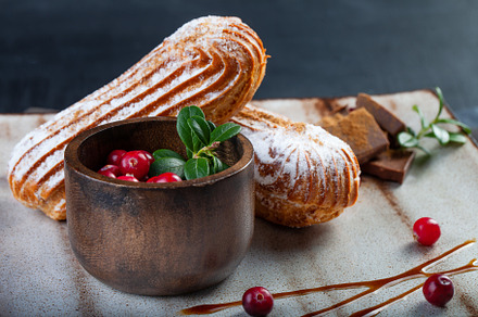Cream eclairs choux pastries served with fresh cranberries on a