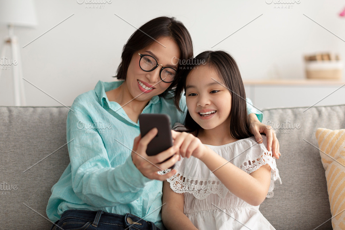 Loving Asian grandmother and her cute little granddaughter using smartphone on, a Photo by Prostock-Studio (Photo 2 of 2)