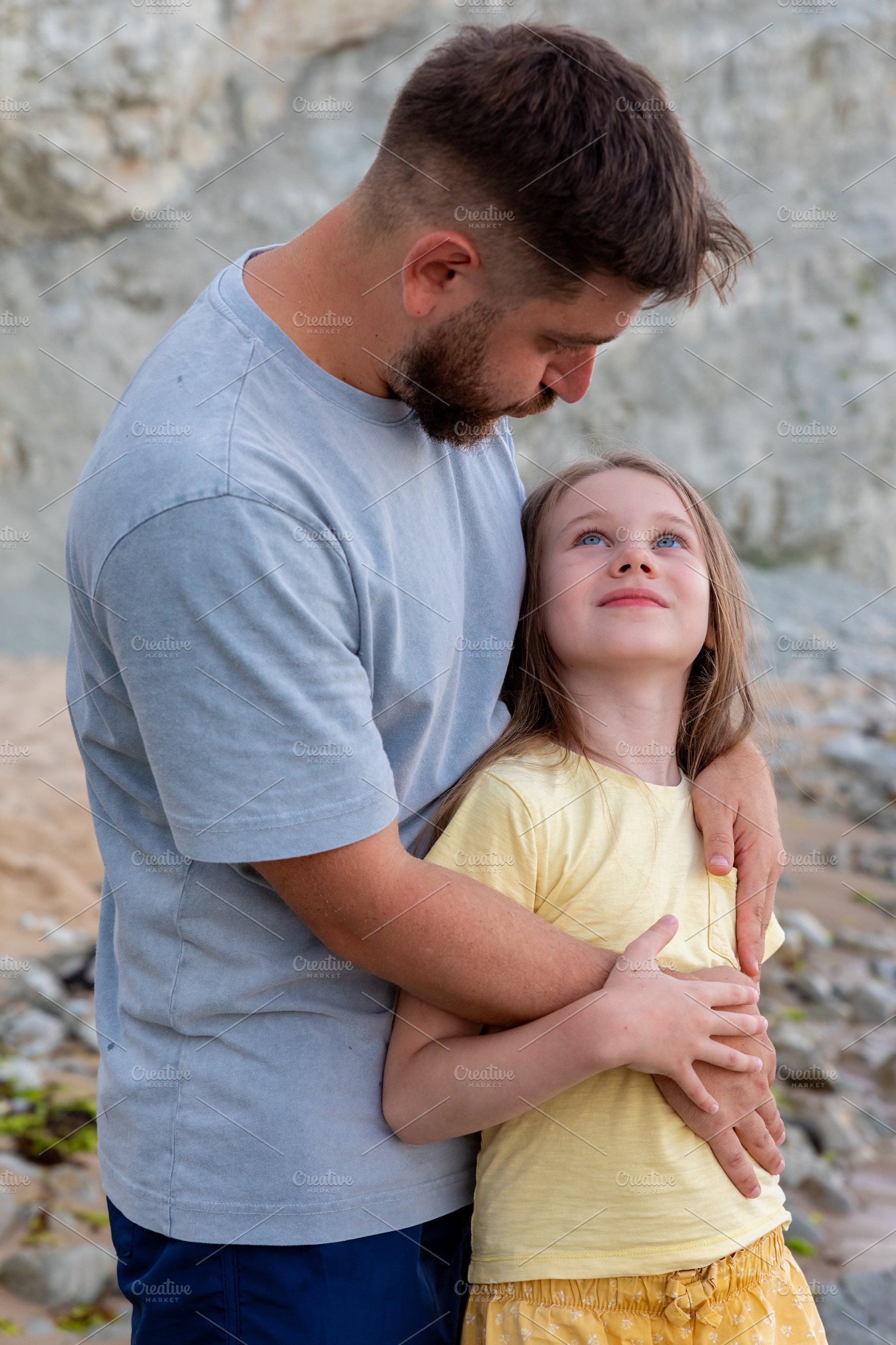 Loving father hugging his smiling daughter outside on a rocky beach, showing fa, a Person Photo by Ales Munt