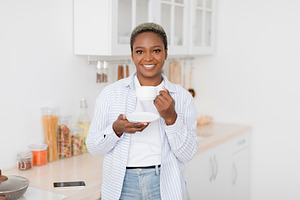 Cheerful pretty millennial black female in casual clothes drinking her favorite, a Person Photo by Prostock-Studio