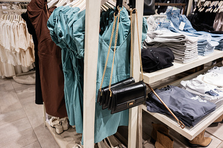 Clothing store interior with dresses and bags displayed on shelves and racks, a Photo by AS photostudio