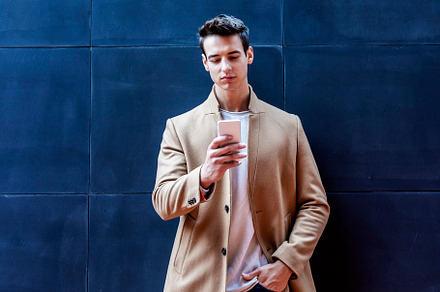 Handsome man wearing a coat standing outdoors, holding mobile phone, a Person Photo by 2Design