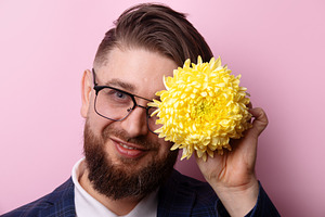Cheerful bearded man in glasses holding a bright yellow flower n, a Person Photo by Ales Munt