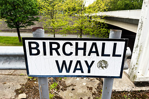 Birchall Way street sign on a worn metal post near an overpass i