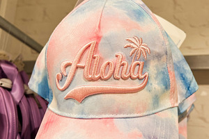 Colorful tie dye cap with 'Aloha' text displayed in a retail store, a Photo by AS photostudio