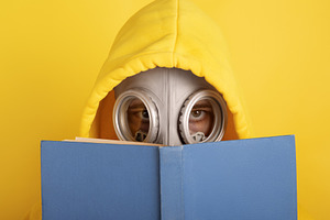 Person in a yellow hoodie and gas mask reading a blue book again, a Person Photo by Ales Munt