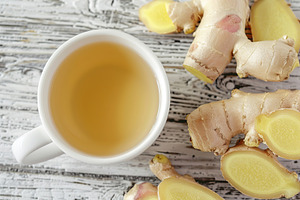 Cup of ginger tea with sliced ginger root on wooden table, a Food & Drink Photo by AlyaAnd