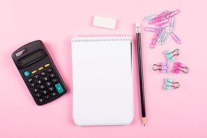 Notebook next to clips calculator, and pencil on pink background. Back to school concept.