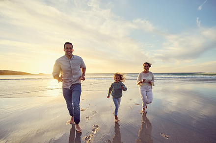 Carefree mixed race family running and having fun together on the beach. Parents spending time with their daughter while on holiday. Happy little girl smiling and bonding with her parents on vacation, a Photo by Peopleimages.com