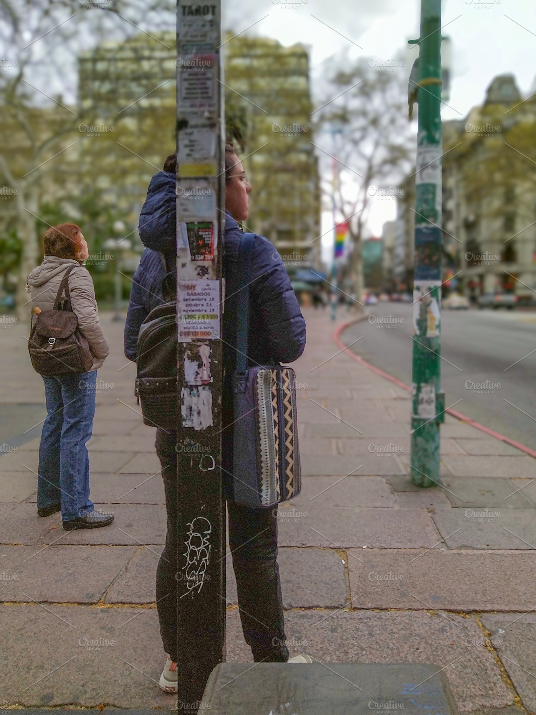 Two women standing on sidewalk waiting for public bus, a Person Photo by DanFLCreativo