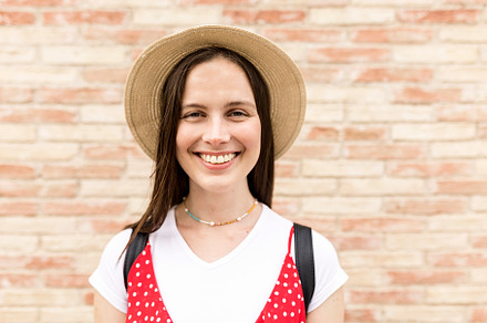 Young female tourist smiling while looking at camera in front of wall - Portrai, a Holiday Photo by Xavier Lorenzo