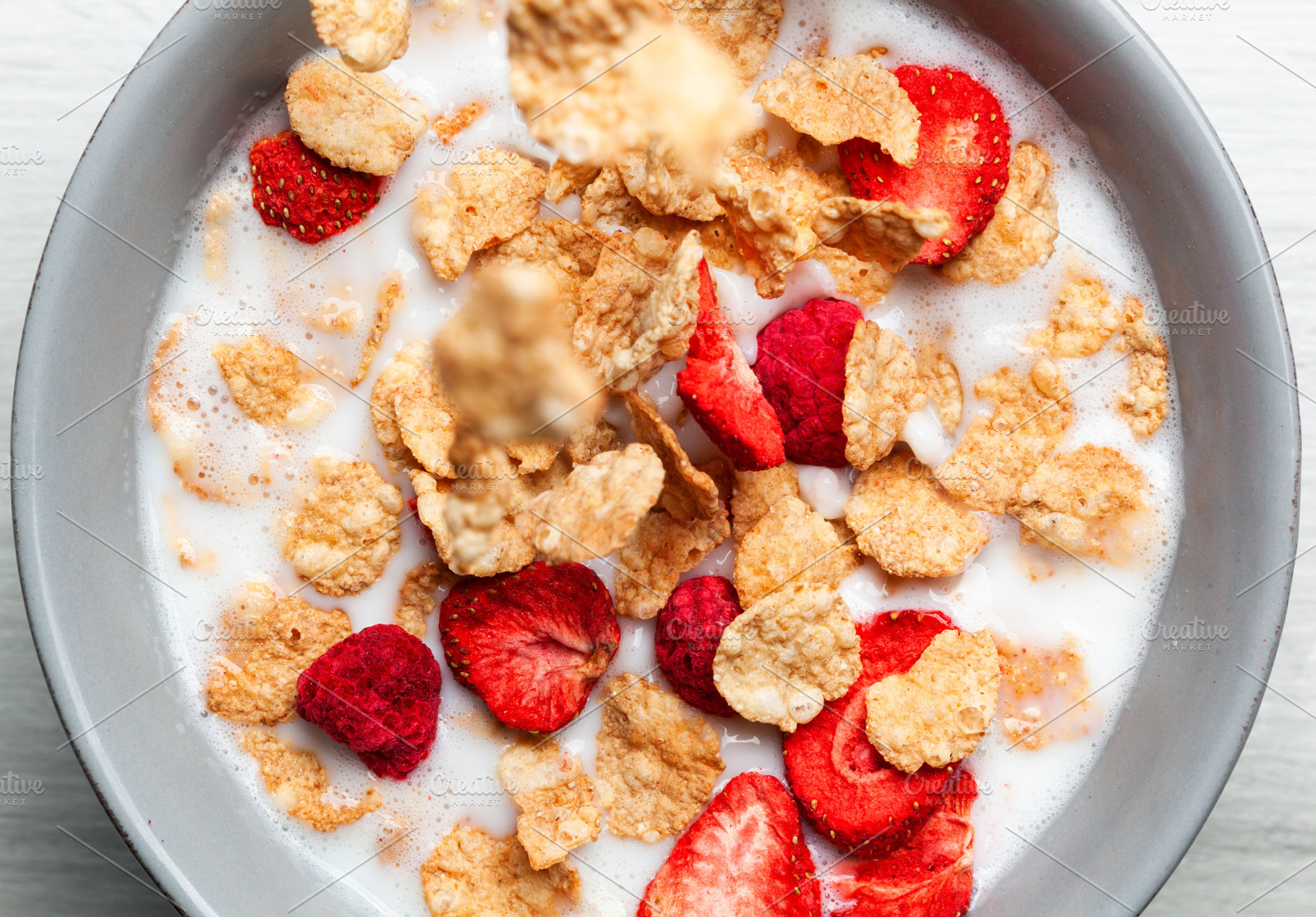 Cornflakes and freeze dried berries falling into a bowl of milk creating a heal, a Food & Drink Photo by Antonio Gravante Market