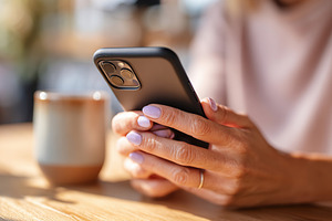 Woman using smartphone while seated at a wooden table in a cozy cafe environmen, a Photo by AlyaAnd