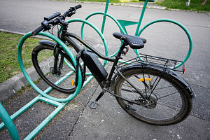 Modern electric bicycle parked in a public bike rack on an urban street, a Photo by AS photostudio