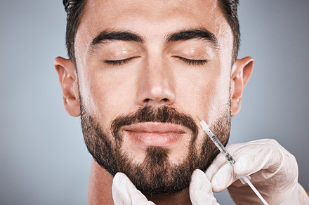 Needle, man and plastic surgery for skincare, collagen and beauty clinic in studio. Botox cosmetics, face injection and male aesthetic for body transformation, change and facial filler on background, a Photo by Peopleimages.com