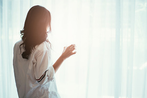 Woman holding a glass of water while looking out of the window - back of silhouette woman, a Person Photo by Twinster Photo