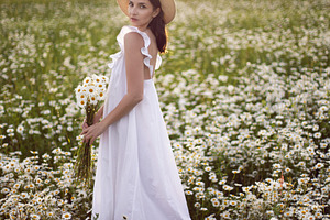 beautiful young brunette woman with long hair in a hat and a white dress is hol