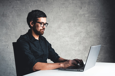 A man sits with a laptop in a black