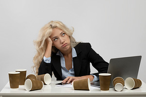 Exhausted woman office employee sitting at workplace surrounded by coffee cups,, a Photo by Prostock-Studio