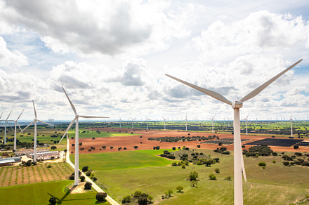 Drone shot of wind turbines turning slowly across vast green fields under cloud