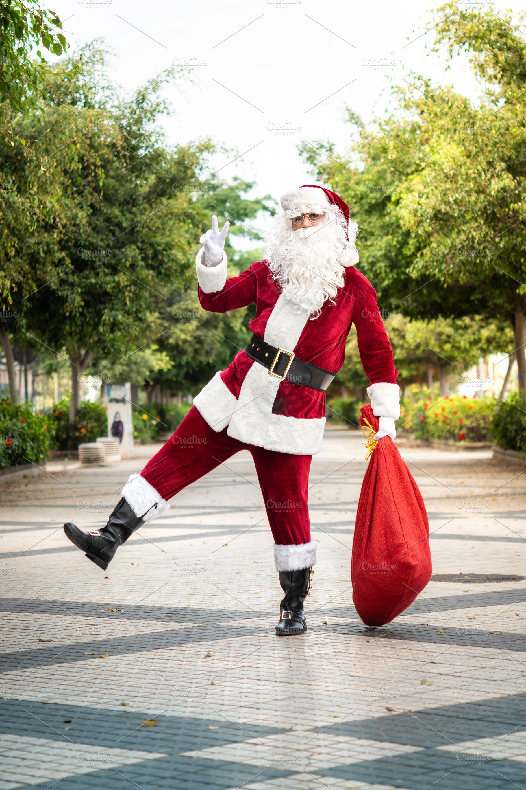Playful Santa Claus carrying gift sack and making peace sign outdoors, a Person Photo by etorres69