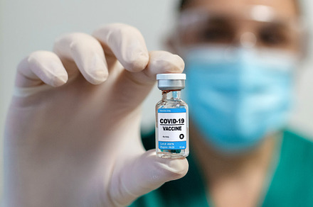 Female laboratory technician showing vial of coronavirus vaccine, a Health & Medical Photo by davidpereiras