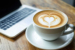 Coffee with latte art beside a lapto, a Photo by Tanuart