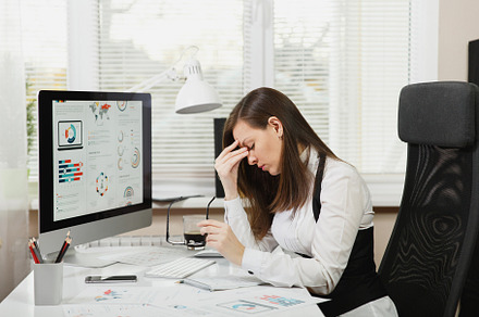 Beautiful tired perplexed and stress brown-hair business woman in suit and glasses sitting at the desk with cup of coffee, working at contemporary computer with documents in light office, a Person Photo by ViDi Studio