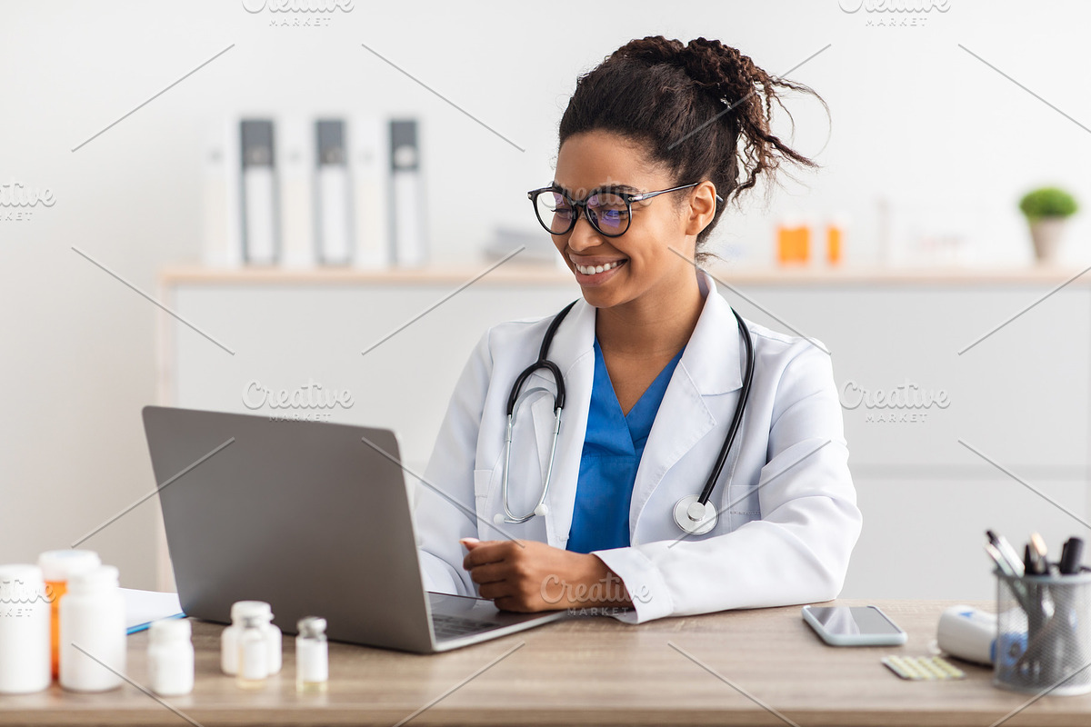 Portrait of smiling doctor looking at screen sitting at desk, a Photo by Prostock-Studio (Photo 2 of 2)