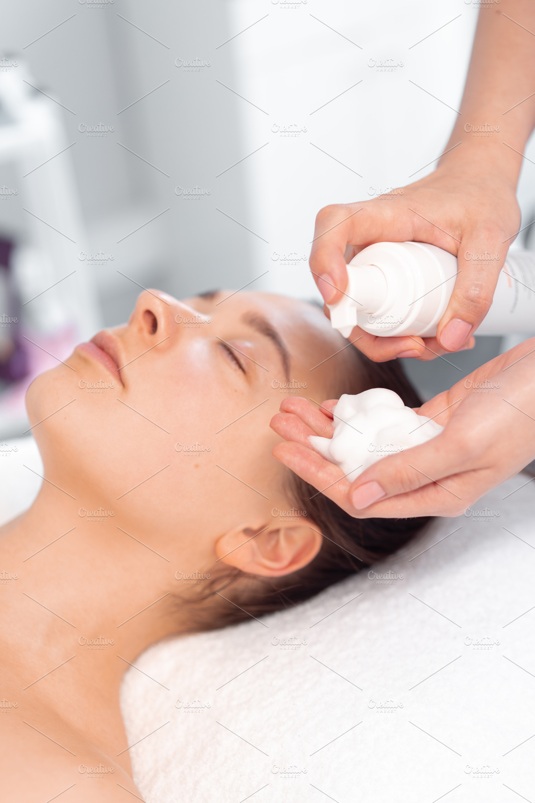 Therapist taking foam cream in hand while massaging woman's face, a Person Photo by andreonegin market