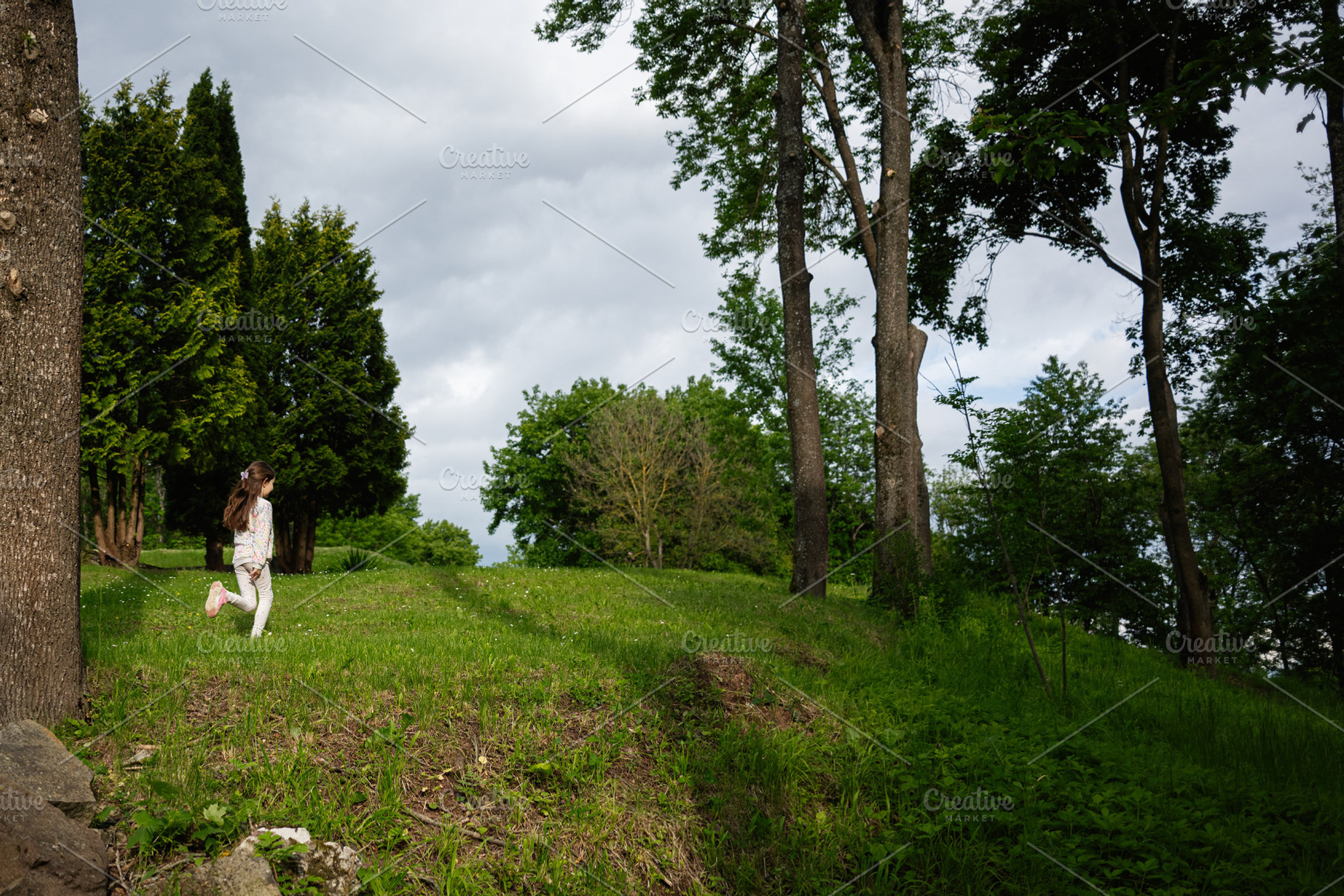 Young girl playing outdoors surrounded by green trees and natural landscape, a Person Photo by AS photostudio