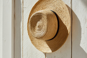 Straw sunhat hanging on wooden wall, a Photo by Virgo Studio
