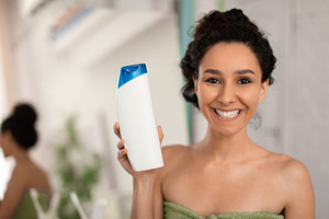 Smiling woman showing shampoo bottle with mockup for design at camera, advertis, a Photo by Prostock-Studio