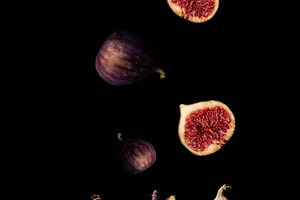 Ripe whole and sliced figs flying over a wooden board on a black, a Food & Drink Photo by ndanko